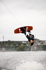 view of female wakeboarder holds rope and doing flips and jumping over the water on wakeboard