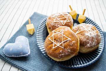 Happy Hanukkah. A traditional treat of doughnuts with David star and dreidel made from cheese and biscuit sticks. Blue fabric heart decor. Copy space