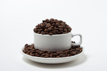 White cup overflowing with coffee beans on a white background. Freshly roasted coffee beans