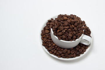 White cup overflowing with coffee beans on a white background. Freshly roasted coffee beans