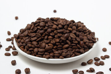 A plate overflowing with coffee beans on a white background. Freshly roasted coffee beans