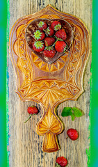 Fresh red strawberries in a heart-shaped wooden plate on a carved wooden kitchen board, on a green background