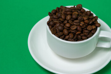 Cup filled with coffee beans on a green background. Freshly roasted coffee beans. Excessive consumption of caffeine
