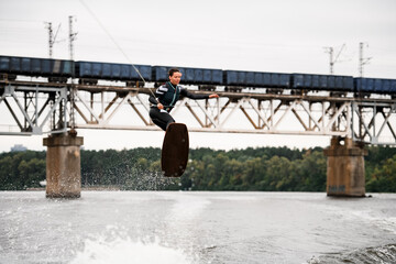 young sportive woman holding rope and professionally jumping over splashing water on wakeboard