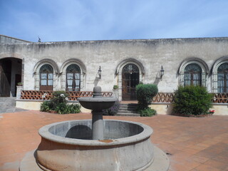 Entrada de hacienda antigua con largos ventanales, balcón y fuente en medio