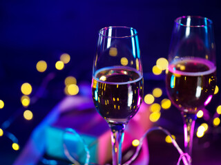 Two glasses of wine or champagne on a neon background, Christmas decor, bokeh lights garlands