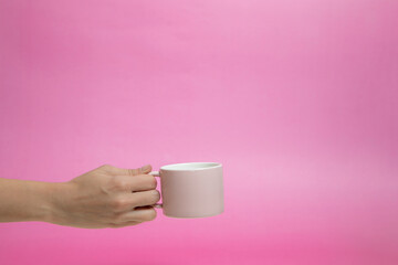 Pink cup, mug in hand. Pink background. Morning coffee.