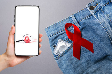 Know your status. Jeans with a condom in the pocket and a red ribbon. Close up. Gray background. The concept of world AIDS day and safe sex