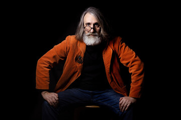 Portrait of a mature man in a stylish orange jacket on a black background . A fashionable intellectual looks into the camera with mockpice and interest. 