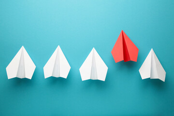 Red paper plane leading white ones on blue background, leadership concept