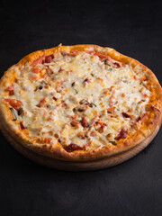 Delicious traditional homemade pizza with tomato, pepper, sausage, cheese on a black background.