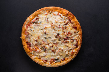Delicious traditional homemade pizza with tomato, pepper, sausage, cheese on a black background.
