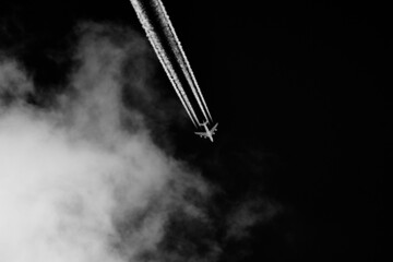 Airplane leaves contrails in the sky with clouds on black background.