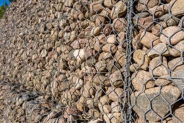 engineering structure made of stones behind metal wire netting to strengthen the river bank near the road bridge