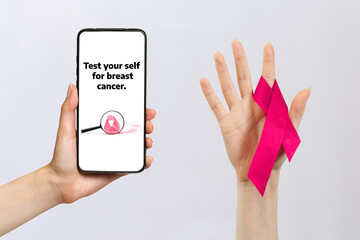 Female hand on the right with a pink ribbon. The hand on the left holds a smartphone. Gray...