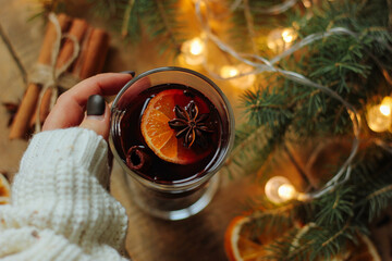 Female hands holding mug with mulled wine above wooden table. Top view