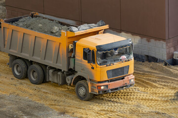 The truck is carrying a full body of rubble. The truck drives on a sand-covered construction site. Transportation of building materials.