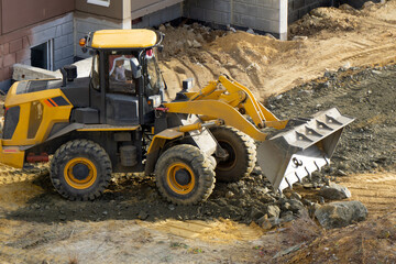 Bulldozer unloads gravel at a construction site. A tractor with a bucket spreads gravel and sand.