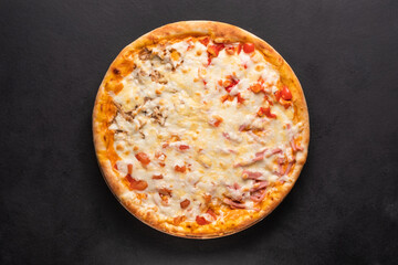 Delicious traditional homemade pizza with tomato, pepper, sausage, cheese on a black background.