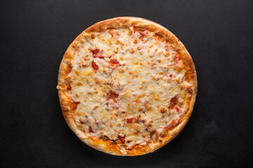 Delicious traditional homemade pizza with tomato, pepper, sausage, cheese on a black background.