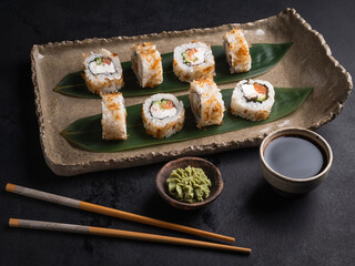 Sushi with red fish, cucumber, cream cheese on a clay plate, soy sauce, wasabi.