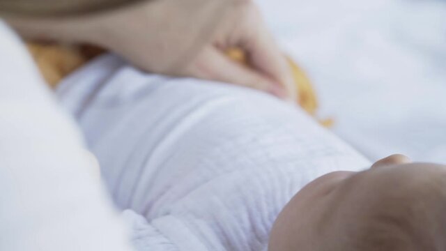 Unrecognizable woman dresses little baby in sleeper carefully on large bed in bedroom at home extreme close-up view wother and child hands