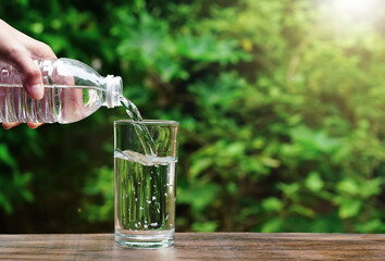 slow motion of pouring water from the bottle into a glass on wooden in nature on green background. Concept of environment protection, healthy drink.	