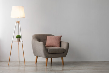 Comfortable armchair with pink pillow, glowing lamp on floor on gray wall background in office or living room