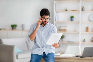 Work from home. Young arab entrepreneur talking with colleague on cellphone and checking financial...