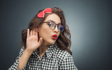 Close up woman holding palm near his ear trying to listen something interesting over dark gray -...