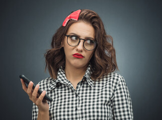 Annoyed girl on the phone over dark gray - black background. Annoying young woman using mobile...
