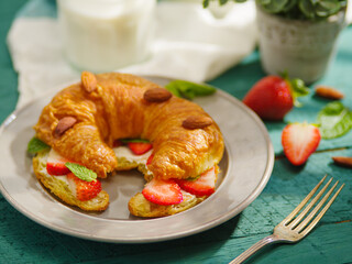 Continental breakfast for one person. Fragrant croissant with strawberries, mint, almonds, fork, milk, decor. Close-up. Restaurant, hotel, cafe, pastry shop, home cooking.
