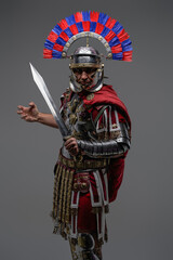 Proud roman soldier posing against gray background holding sword