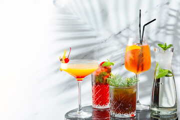set cocktails on marble table and light background banner. five kinds of colorful summer cocktails in glasses and shadow of tropic branch on background. Mojito, Aperol Spritz, margarita