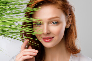 Naklejka premium Ginger-Haired Girl Posing With Green Grass Near Face, Gray Background