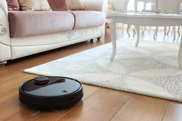 Black robot vacuum cleaner in living room.  Modern Turkish house with furnitures. Technological home appliances concept.