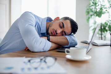 Tired Arab businessman sleeping on his desk in front of laptop, overworking, feeling exhausted in modern office