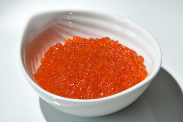 Red caviar in a ceramic cup on a white background. Selective focus. 