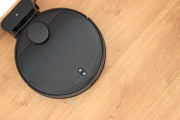Top view of black robot vacuum cleaner with charging stand on wooden laminate. Smart autonomous...