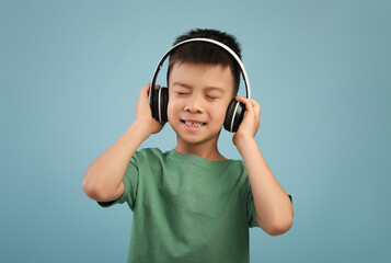 Cheerful little asian boy listening to music in wireless headphones