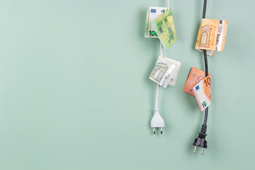 Electric power plugs with Euro banknotes on them hanging on light green background. Energy...