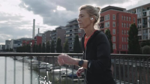 Senior sportswoman in earphones jogging at urban area