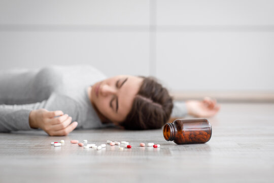 Sad european millennial lady unconscious lying on floor with scattered pills, committed suicide at home