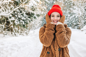 Skin protection in winter frosty time concept. A young attractive woman holding frozen cheeks in a winter park. 