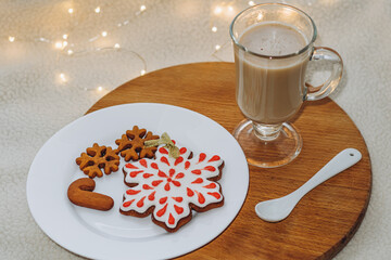 Christmas composition with gingerbread cookies and coffee on a wooden board. Delicious food on a plate. Cozy festive atmosphere. Milk textured background with sweater.