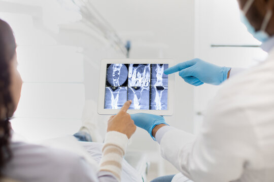 Dentist And Female Patient Looking At Teeth Xray Picture On Digital Tablet