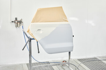 Painting the rear door of the car in special painting chamber. Car service station. Restoring a car after an accident