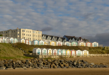 Rows of iconic colourful beach huts banked upon a hillside above a Cornish beach. Blue sky with...