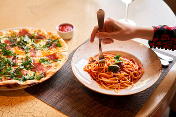 Woman eats Italian pasta with tomato, meat. Close-up spaghetti Bolognese wind it around a fork with...