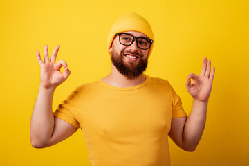 smiling bearded man in glasses showing ok gesture over yellow background